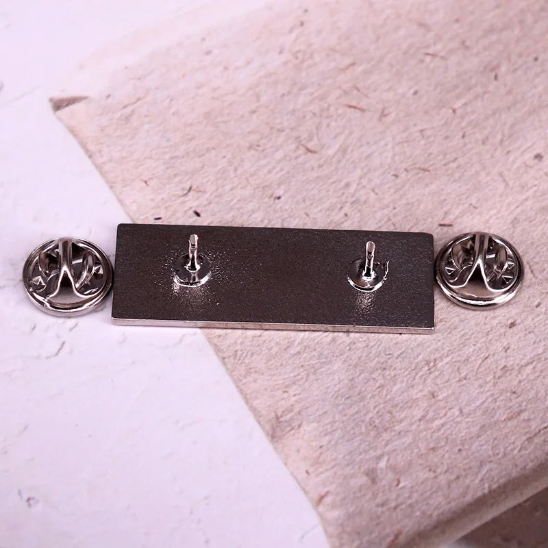 Metallic badge with four hooks on a textured surface