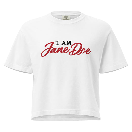 A white short-sleeve crop top t-shirt featuring the text 'I AM Jane Doe' printed on the chest, with 'I AM' in black block letters and 'Jane Doe' in a red cursive script, shown against a plain white background.
