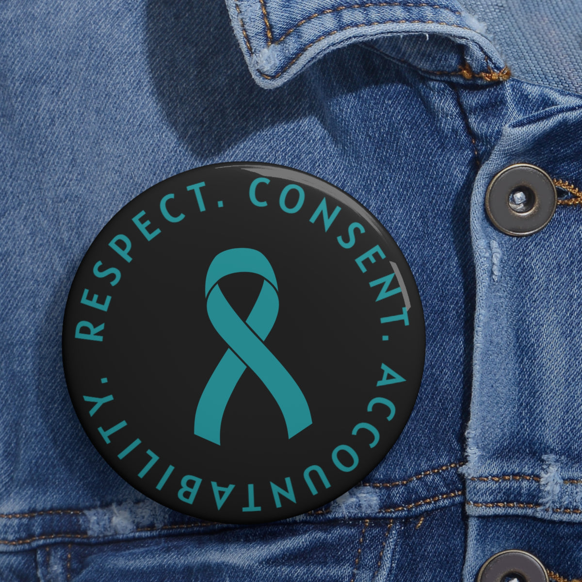 A round black pin-back button with a teal ribbon in the center and the words 'RESPECT. CONSENT. ACCOUNTABILITY'