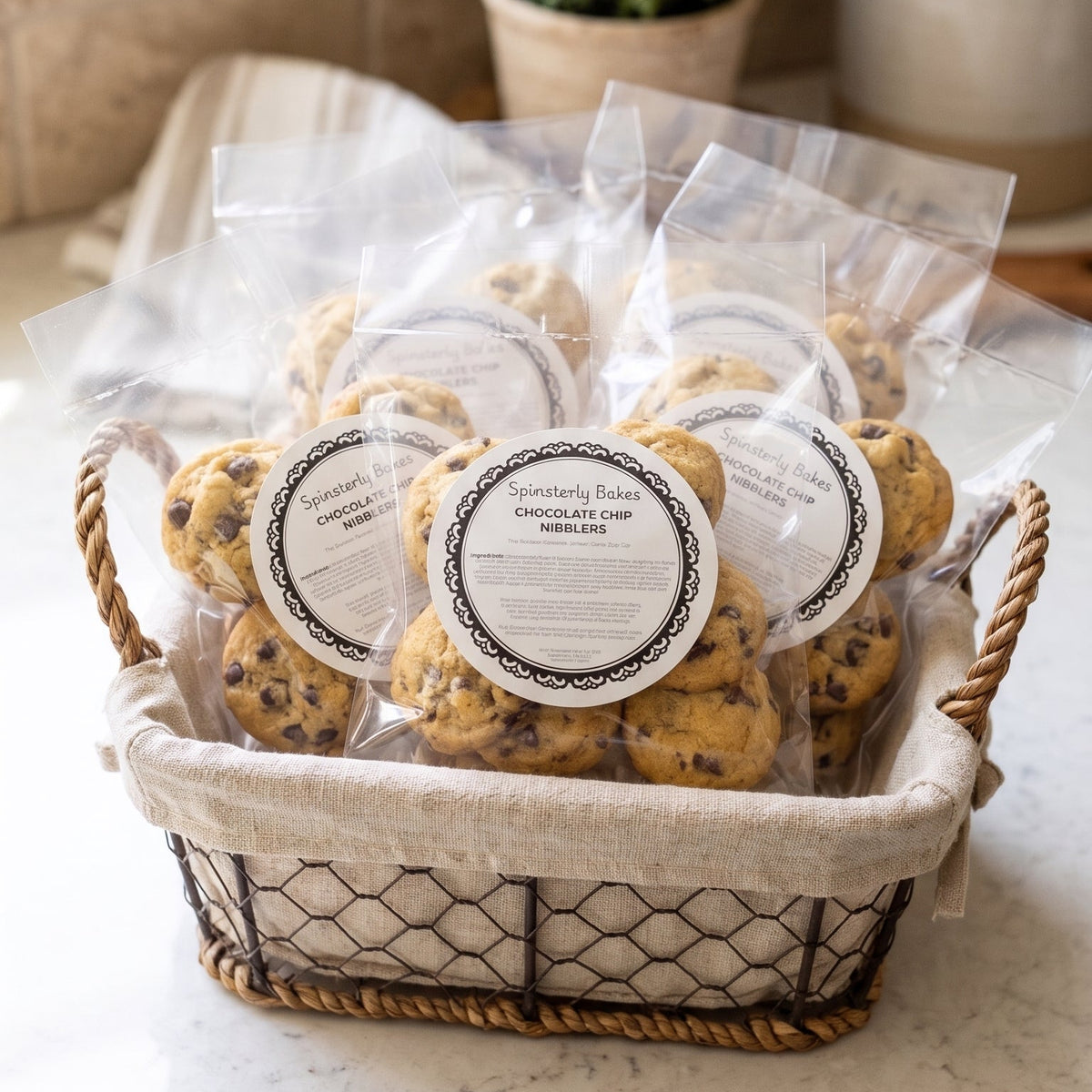 Individual packets of mini chocolate chip cookies, resting in cute basket, resting on a clean, white marble counter.
