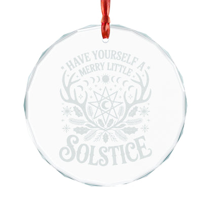 A round clear glass Christmas ornament with a red hanging ribbon, featuring a light gray frosted design with the words 'HAVE YOURSELF A MERRY LITTLE SOLSTICE' and a winter solstice motif including antlers, a moon, and holly.