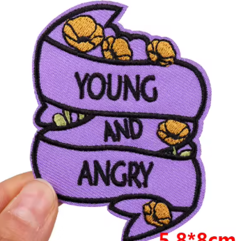 A hand holds a purple embroidered patch with black text reading 'YOUNG AND ANGRY' and small yellow flower motifs, shown on a white background with a red size label '5.8*8cm'.
