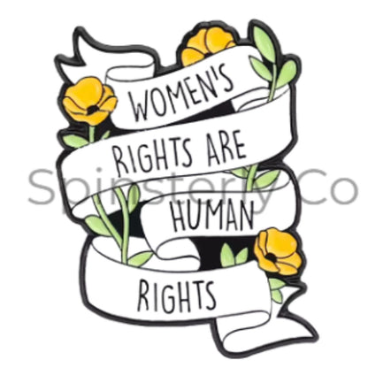 A graphic enamel lapel pin featuring a white banner with the text 'WOMEN'S RIGHTS ARE HUMAN RIGHTS' in black lettering, decorated with yellow flowers and green leaves on a white background.