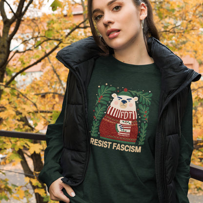 A woman wearing a dark green graphic t-shirt with a festive bear design and the text 'RESIST FASCISM', layered under an open black puffer jacket, set against an outdoor autumn background with yellow foliage.