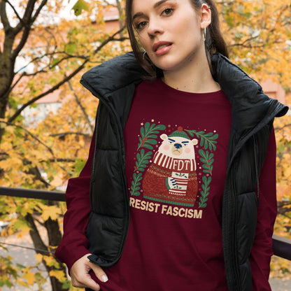 A woman wearing a burgundy crewneck sweatshirt with a festive graphic of a polar bear and the text 'RESIST FASCISM', layered under a black puffer vest, set against a background of autumn trees.
