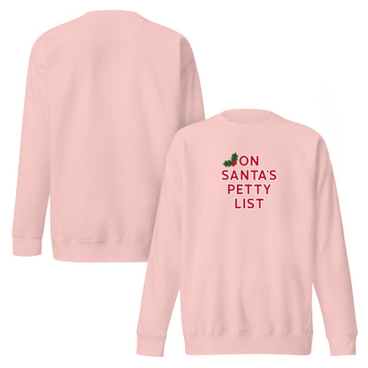 A light pink crewneck sweatshirt shown from both the front and back. The front features a red graphic print that reads 'ON SANTA'S PETTY LIST' next to a small green holly leaf illustration.