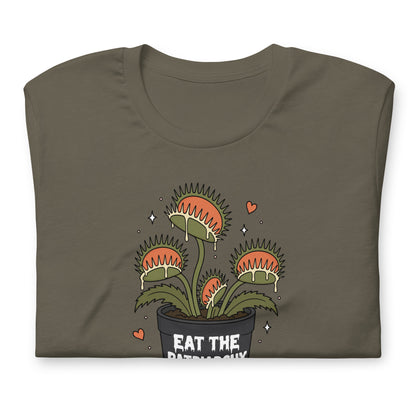 A folded dark olive green t-shirt featuring a cartoon graphic of a potted Venus flytrap with the text 'EAT THE PATRIARCHY' on the front, set against a plain white background.