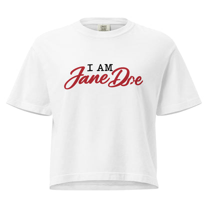 A white short-sleeve crop top t-shirt featuring the text 'I AM Jane Doe' printed on the chest, with 'I AM' in black block letters and 'Jane Doe' in a red cursive script, shown against a plain white background.