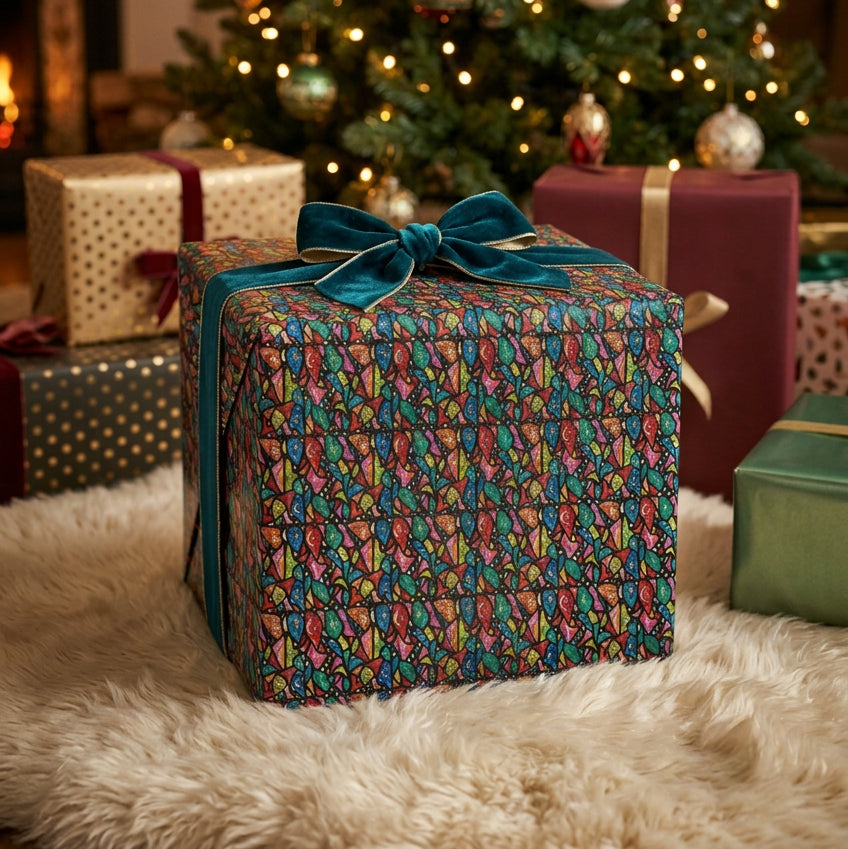A holiday gift box is featured prominently with a stained glass inspired design, with a Christmas tree and other gifts behind it.